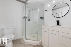 Bathroom featuring a corner glass-enclosed shower, white vanity with integrated sink, black wall-mounted faucet, and round black-framed mirror - 