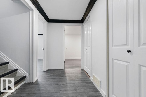 Hallway featuring wood-finish flooring, white paneled doors, and contrasting black trim - 27 Apache Crescent, Leduc, AB 