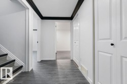 Hallway featuring wood-finish flooring, white paneled doors, and contrasting black trim - 