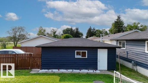 Detached garage featuring dark blue siding, a white service door, and a single window - 27 Apache Crescent, Leduc, AB 