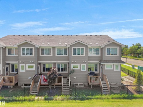 Townhome exterior featuring light grey siding, multiple windows, a brown shingle roof, and individual rear decks with wood railings and stairs - #30 4137 76 St Nw, Edmonton, AB 