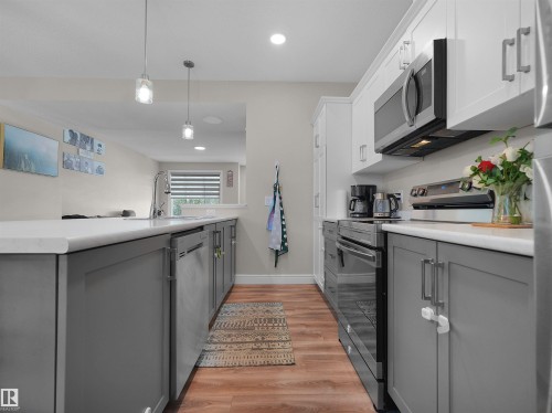 Modern kitchen featuring two-tone cabinetry with white upper and gray lower cabinets, stainless steel appliances, white countertops, and wood-finish flooring - #30 4137 76 St Nw, Edmonton, AB 