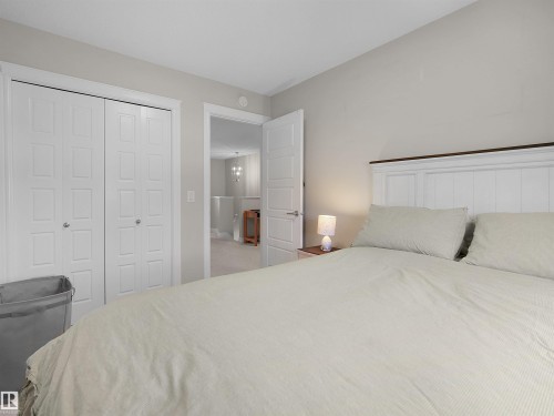 Bedroom featuring a white paneled headboard with a dark wood-finish trim, light gray wall paint, and a double-door closet with white paneled bifold doors - #30 4137 76 St Nw, Edmonton, AB 