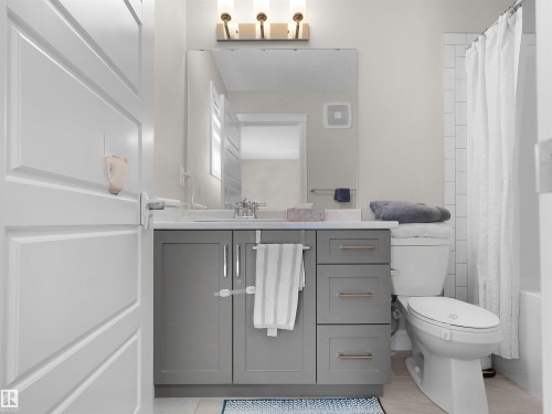 Bathroom featuring a gray vanity with a light-toned countertop, a large mirror, a toilet, and subway tile shower surround - #30 4137 76 St Nw, Edmonton, AB 