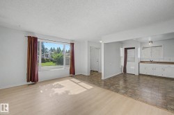 Open concept living area featuring a large picture window, light wood-finish flooring, and white painted walls - 