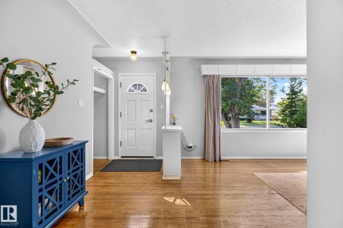 Bright entry area featuring wood-finish flooring, a white paneled entry door with an arched glass insert, and a large window providing ample natural light - 16152 110B Avenue Nw, Edmonton, AB - Indoor Photo Showing Other Room