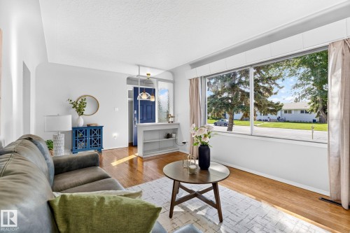 Living area featuring expansive front window, hardwood-finish flooring, white wall tones, and recessed entry nook with built-in shelving - 16152 110B Avenue Nw, Edmonton, AB - Indoor Photo Showing Living Room