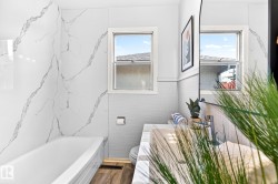 Contemporary bathroom featuring a tub with large format marble-look wall tiling, wood-finish flooring, a white vanity with an integrated sink, and dual windows - 