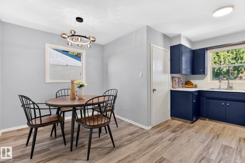 Kitchen and dining area featuring wood-finish flooring, a contemporary chandelier, white trim throughout, and deep blue cabinetry with a stainless steel sink - 16152 110B Avenue Nw, Edmonton, AB - Indoor