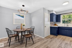 Kitchen and dining area featuring wood-finish flooring, a contemporary chandelier, white trim throughout, and deep blue cabinetry with a stainless steel sink - 