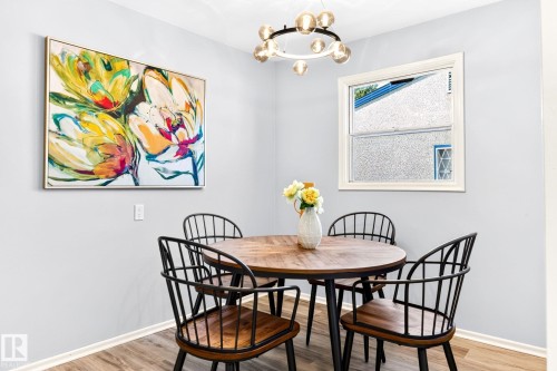 Dining area featuring a contemporary chandelier, wood-finish flooring, a white-framed window, and light gray wall tones - 16152 110B Avenue Nw, Edmonton, AB - Indoor Photo Showing Dining Room