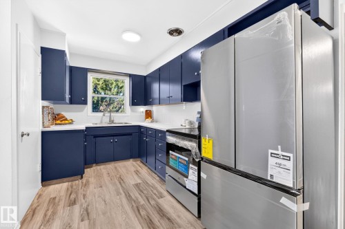 Kitchen featuring blue cabinetry, wood-finish flooring, white countertops, and stainless steel appliances - 16152 110B Avenue Nw, Edmonton, AB - Indoor Photo Showing Kitchen