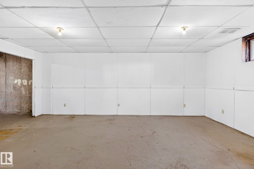 Unfinished lower level space featuring panel walls, two overhead light fixtures, a drop ceiling, and a visible window opening - 16152 110B Avenue Nw, Edmonton, AB - Indoor