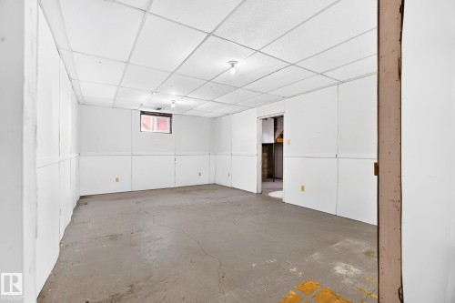 Spacious room featuring paneled walls, a drop ceiling, bare concrete flooring, a small window, and exposed overhead lighting - 16152 110B Avenue Nw, Edmonton, AB - Indoor Photo Showing Other Room