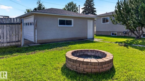 Expansive backyard featuring a circular paver fire pit and a detached garage with a white panel door - 16152 110B Avenue Nw, Edmonton, AB - Outdoor