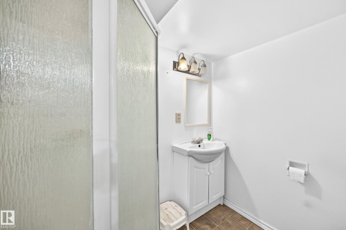 Shower enclosure with textured glass paneling, a white vanity with integrated sink, coordinating wall mirror, three-light vanity fixture, and brown tile flooring - 243 Abbotsfield Road Nw, Edmonton, AB - Indoor Photo Showing Bathroom