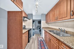 Galley kitchen featuring wood-finish cabinetry, granite-style countertops, stainless steel double basin sink, and wood-finish flooring - 