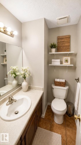 Bathroom featuring a vanity with dark wood-finish cabinetry and a light-toned countertop, a rectangular mirror, a three-light fixture with brushed nickel accents, and warm-toned floor tiles - 1022 106 Street Nw, Edmonton, AB - Indoor Photo Showing Bathroom