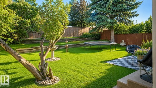 Spacious backyard featuring a lush lawn, mature trees, tiered landscaping with wood retaining walls, and a checkered patio area - 1022 106 Street Nw, Edmonton, AB - Outdoor With Backyard