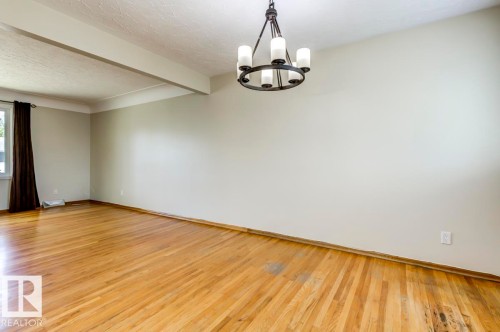 Expansive room featuring wood-finish flooring, a contemporary chandelier light fixture, neutral wall colors, and a large window - 8511 64 Avenue, Edmonton, AB - Indoor Photo Showing Other Room