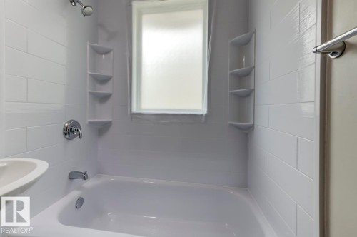 White subway tile surround with integrated corner shelving, white bathtub, chrome shower fixtures, and frosted window - 8511 64 Avenue, Edmonton, AB - Indoor Photo Showing Bathroom