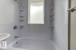 White subway tile surround with integrated corner shelving, white bathtub, chrome shower fixtures, and frosted window - 