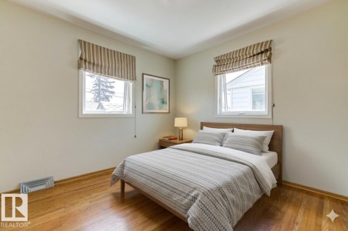 Bedroom featuring two windows with striped Roman shades, wood-finish flooring, and light-toned walls - 8511 64 Avenue, Edmonton, AB - Indoor Photo Showing Bedroom