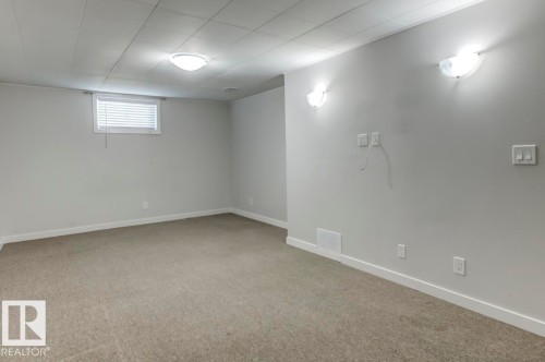 Spacious room with light gray walls, neutral carpet flooring, and a drop ceiling - 8511 64 Avenue, Edmonton, AB - Indoor