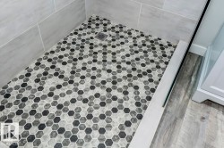 Walk-in shower featuring gray subway tile walls and a hexagonal mosaic tile floor with a central drain - 