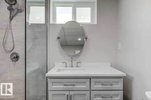 Bathroom featuring a light gray vanity with chrome hardware, an oval mirror, and a white countertop - 8511 64 Avenue, Edmonton, AB - Indoor Photo Showing Bathroom