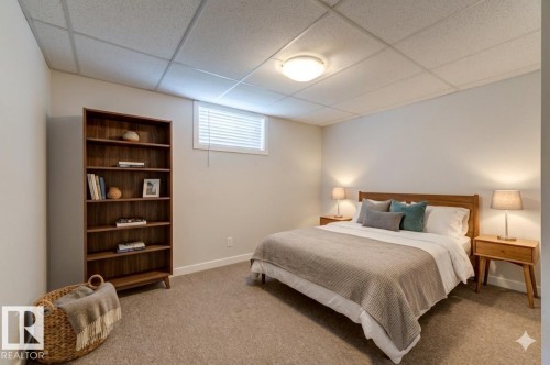 Carpeted room featuring a wood-finish bookcase, white walls, and a drop ceiling with a flush-mount light fixture - 8511 64 Avenue, Edmonton, AB - Indoor Photo Showing Bedroom