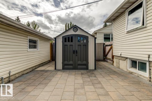 Arched-door storage shed with decorative windows positioned on a stone paver patio - 8511 64 Avenue, Edmonton, AB - Outdoor With Exterior