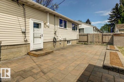 Rear exterior featuring cream-colored siding, a white storm door, and a multi-toned paver patio - 8511 64 Avenue, Edmonton, AB - Outdoor With Exterior