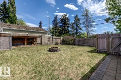 Spacious backyard featuring a block paver fire pit, wood fencing, chain link fencing, a covered storage area, and a paver stone patio - 
