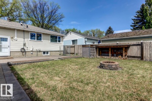 Spacious backyard featuring a stone-clad fire pit, wood privacy fencing, and a built-in wood storage structure - 8511 64 Avenue, Edmonton, AB - Outdoor With Deck Patio Veranda