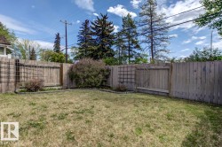 Fenced backyard featuring natural grass, perimeter garden beds, and mature shrubs - 