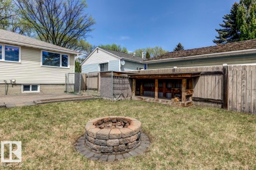 Expansive backyard featuring a stone-paver fire pit, a concrete patio, a wood fence, and a wood storage structure - 8511 64 Avenue, Edmonton, AB - Outdoor