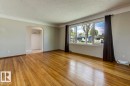 Spacious living area featuring polished wood flooring, a large multi-pane window, neutral wall tones, and crown molding - 8511 64 Avenue, Edmonton, AB  - Indoor Photo Showing Other Room 