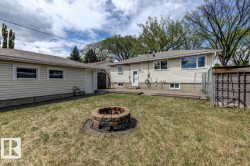 Backyard featuring a stone fire pit, concrete patio, and a detached garage with siding - 