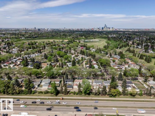 Expansive aerial perspective showcasing a residential area with varied housing styles, mature trees, and a distant city skyline - 8511 64 Avenue, Edmonton, AB - Outdoor With View