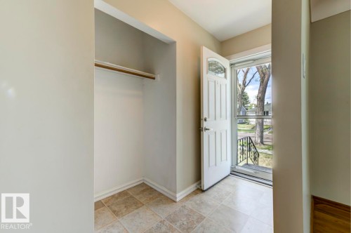 Foyer featuring neutral wall paint, tiled flooring, a built-in coat closet with a hanging rod, a paneled entry door with an arched glass insert, and a screen door - 8511 64 Avenue, Edmonton, AB - Indoor Photo Showing Other Room