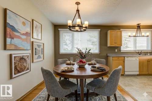 Open-concept dining area featuring a wood-finish flooring, a round dining table, and an overhead chandelier with frosted glass shades - 8511 64 Avenue, Edmonton, AB - Indoor Photo Showing Dining Room