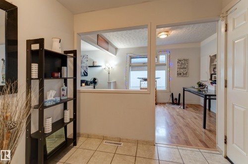Tiled flooring provides a durable entry, leading to an open doorway with wood-finish flooring - 13211 77 Street Nw, Edmonton, AB - Indoor Photo Showing Other Room