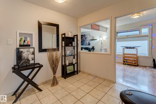 Tiled flooring in a neutral tone, featuring a built-in wall niche, an open pass-through window, and a doorway with wood-finish flooring visible beyond - 13211 77 Street Nw, Edmonton, AB - Indoor Photo Showing Other Room