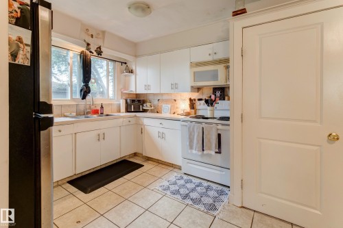 Kitchen featuring white cabinetry with silver hardware, tile backsplash, and light-toned tile flooring - 13211 77 Street Nw, Edmonton, AB - Indoor Photo Showing Kitchen With Double Sink