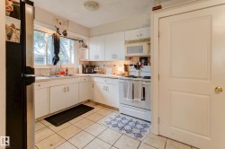 Kitchen featuring white cabinetry with silver hardware, tile backsplash, and light-toned tile flooring - 