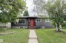 Ranch-style residence featuring dark gray siding, a prominent red entry door, a concrete walkway, a front lawn with mature trees, and multiple windows - 13211 77 Street Nw, Edmonton, AB  - Outdoor With Facade 