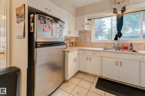 Kitchen featuring white cabinetry, light-toned countertops, a stainless steel refrigerator, and a double basin sink - 13211 77 Street Nw, Edmonton, AB - Indoor Photo Showing Kitchen With Double Sink