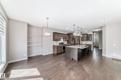 Open-concept living area featuring wood-finish flooring, a contemporary kitchen, and built-in shelving - 
