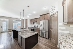 Modern kitchen with dual islands, light wood-finish flooring, stainless steel appliances, pendant lighting, and a subway tile backsplash - 